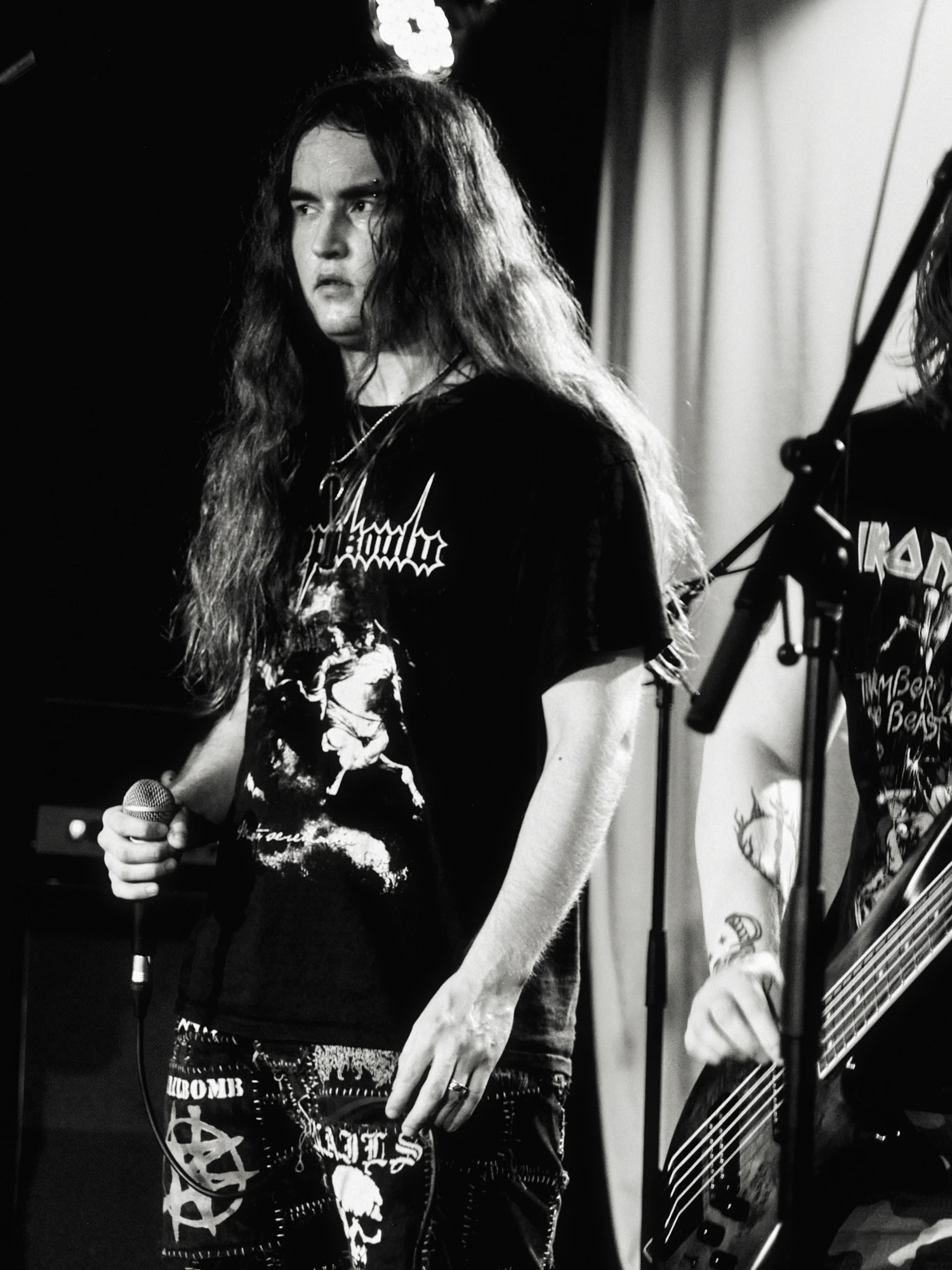 A black and white gig photo of a band performing live on stage. The musicians are captured in action with stage lighting illuminating them.