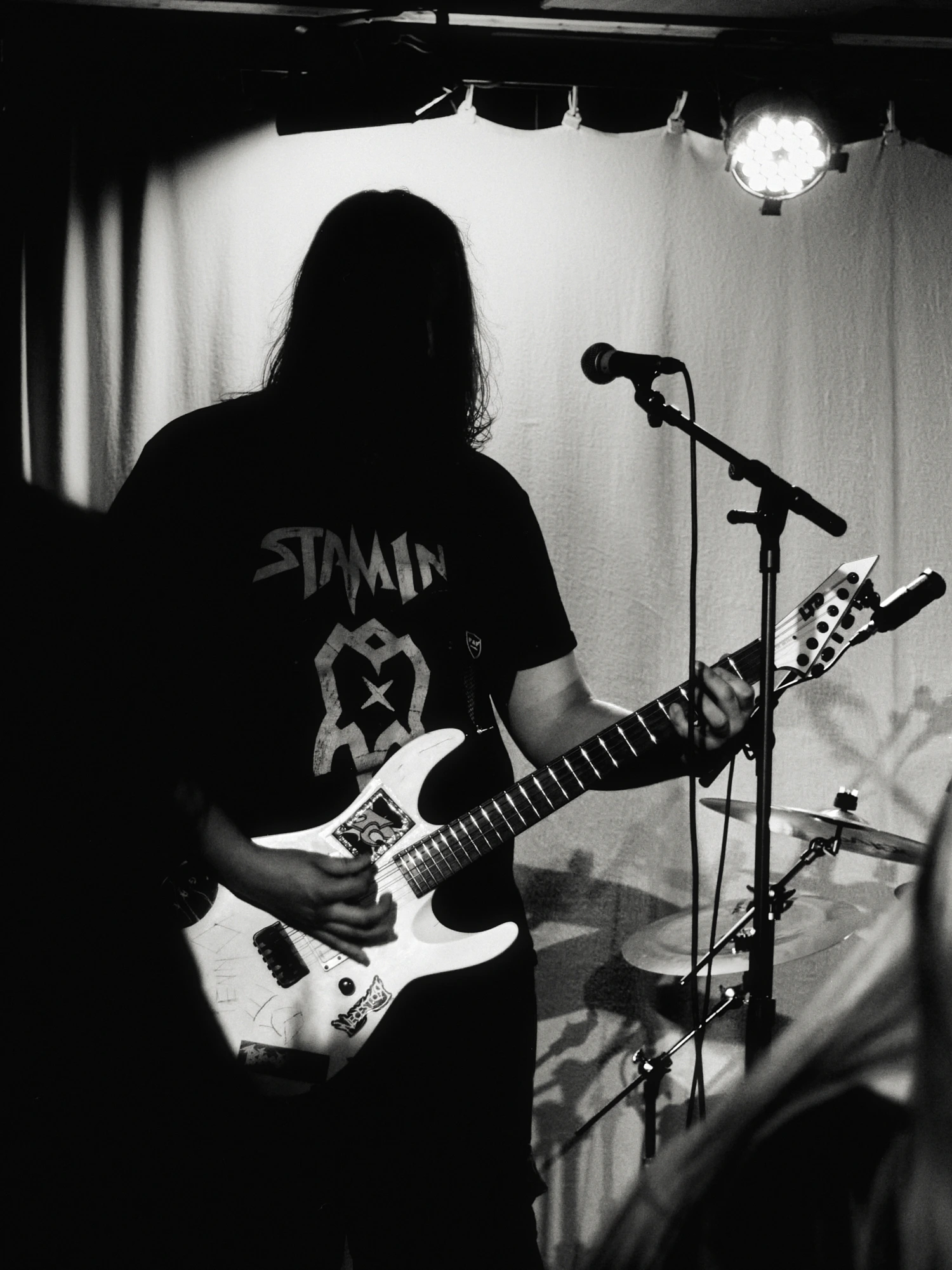 A black and white gig photo of a band performing live on stage. The musicians are captured in action with stage lighting illuminating them.
